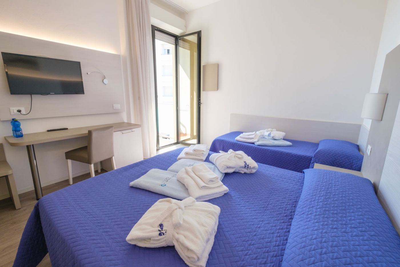 Camera SUPERIOR Luminosa ed elegante camera con letto matrimoniale e singolo con copriletto blu e teli da bagno Camera SUPERIOR Luminosa ed elegante camera con letto matrimoniale e singolo con copriletto blu e teli da bagno