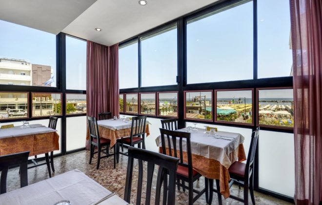 La sala ristorante con i tavoli apparecchiati e ampia vetrata sulla spiaggia