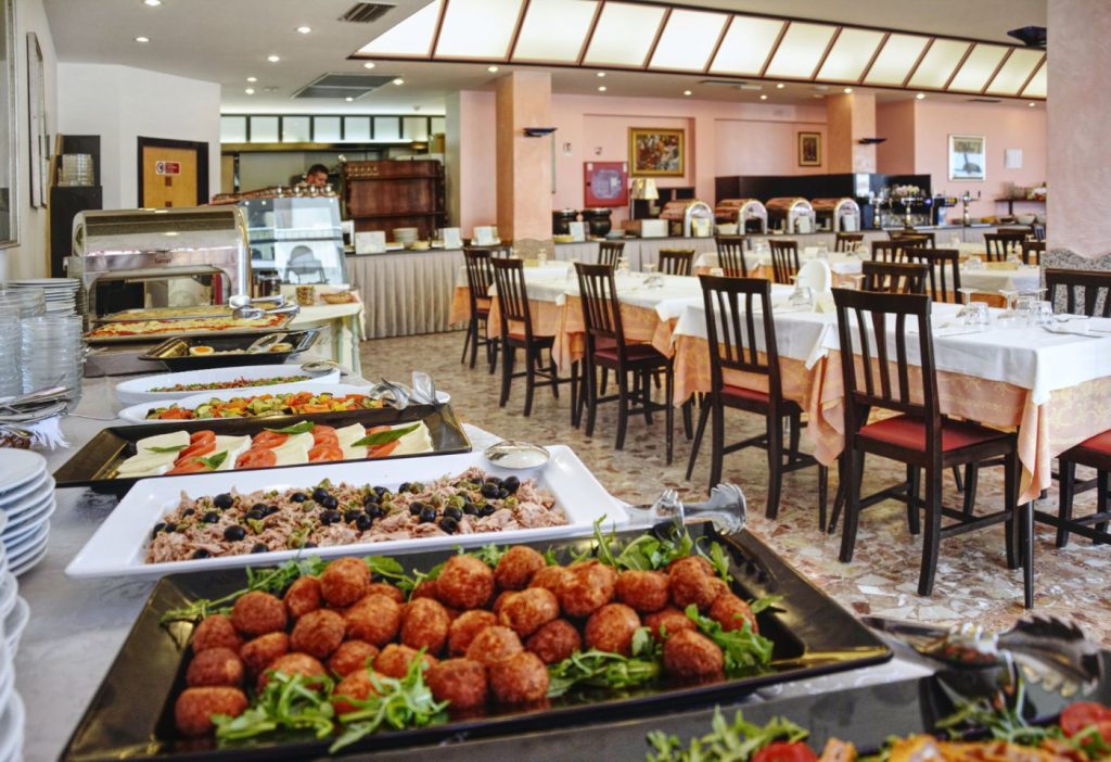 La sala ristorante con i tavoli apparecchiati e ricco buffet in primo piano