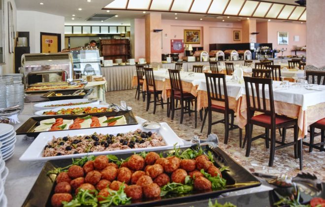 La sala ristorante con i tavoli apparecchiati e ricco buffet in primo piano