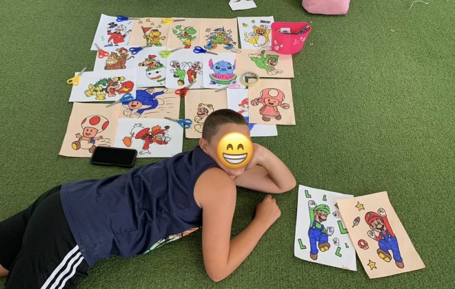 Bambino mostra i propri disegni stesi sul tappeto