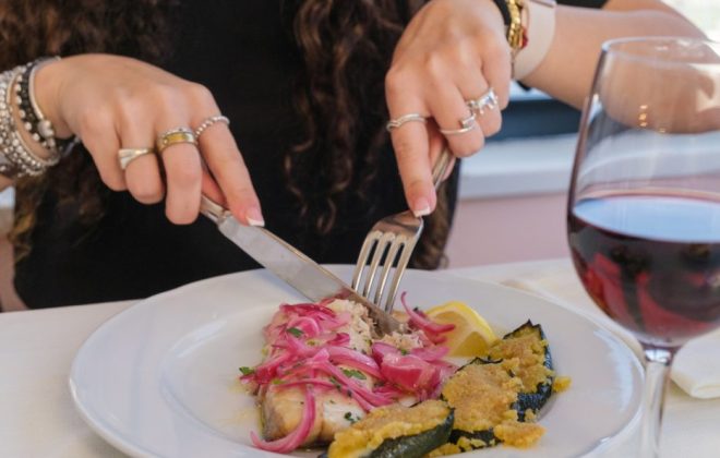 una cliente pranza con un piatto di pesce e verdure gratinate