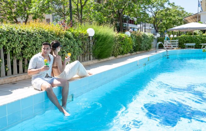 Coppia seduta a bordo piscina con un drink durante una bellissima giornata