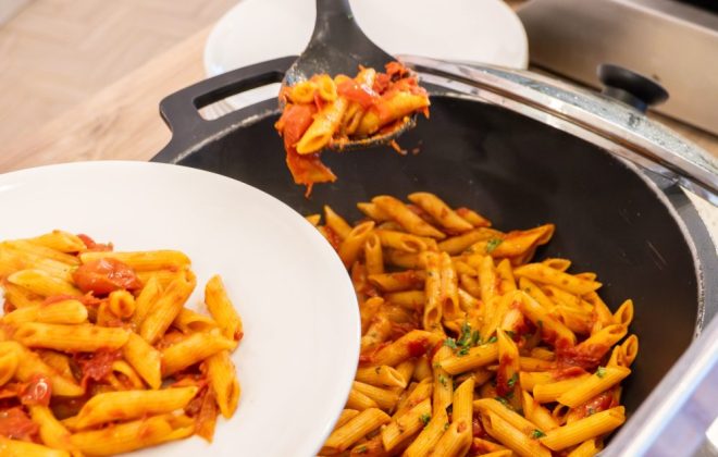 addetto al buffet riempie piatto di pasta pomodoro e gamberetti