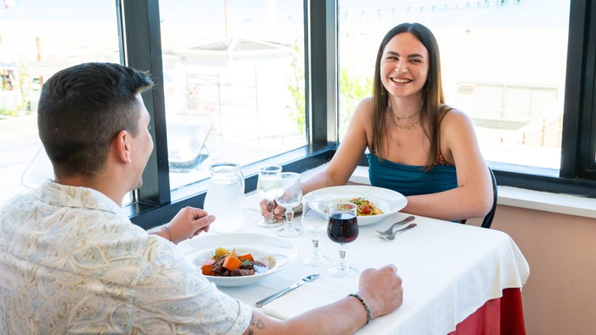 coppia pranza al ristorante davanti a una vetrata panoramica vista spiaggia
