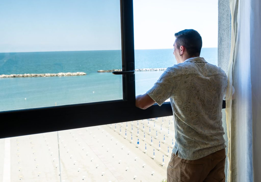 ragazzo che si affaccia dalla finestra e guarda il mare